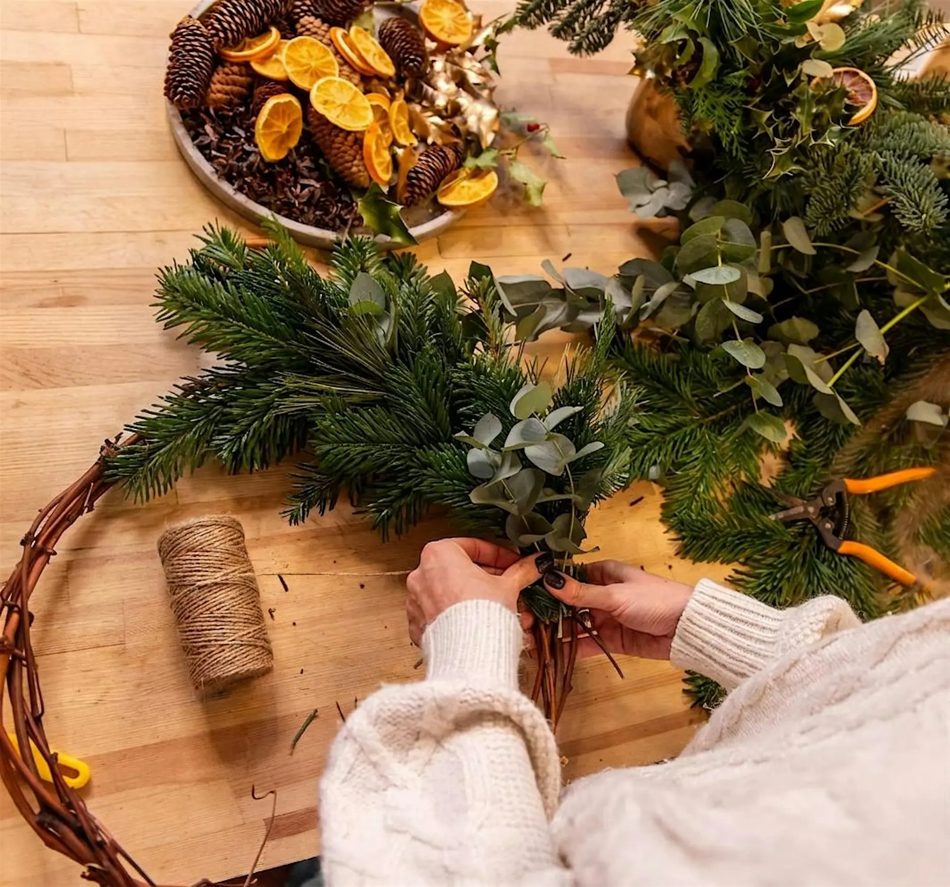 Elaboración artesanal de una corona de Navidad con ramas de abeto, eucalipto y elementos naturales