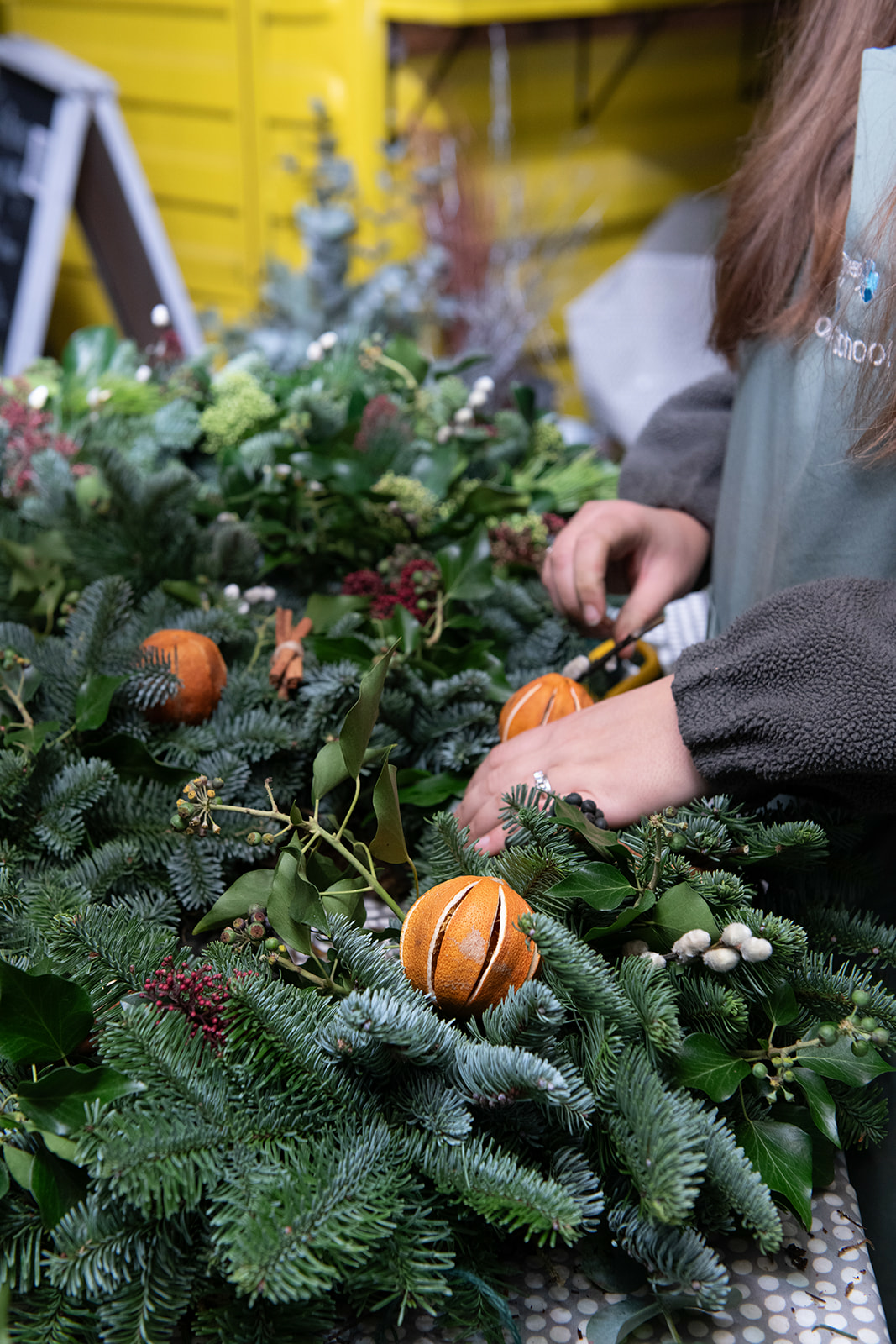 Persona elaborando una corona de Navidad con ramas de abeto, frutos y naranjas secas